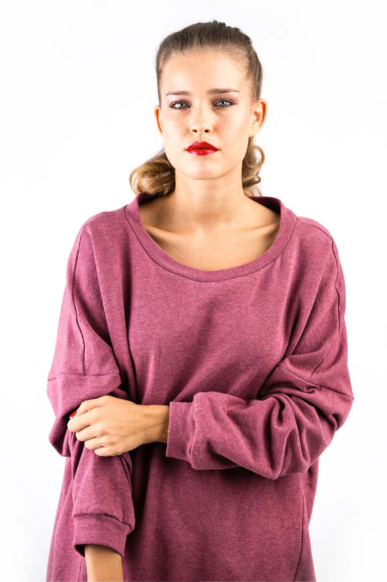 In front of a white wall, a woman with red lipstick is standing, wearing her self-sewn shirt with a round neckline.