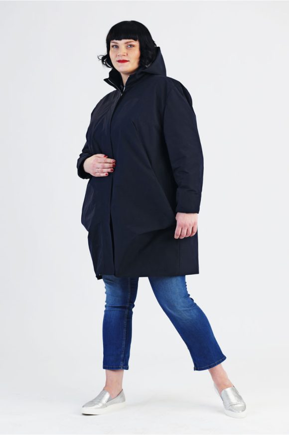 A woman is standing in front of a white wall, wearing her self-sewn parka named Amy.