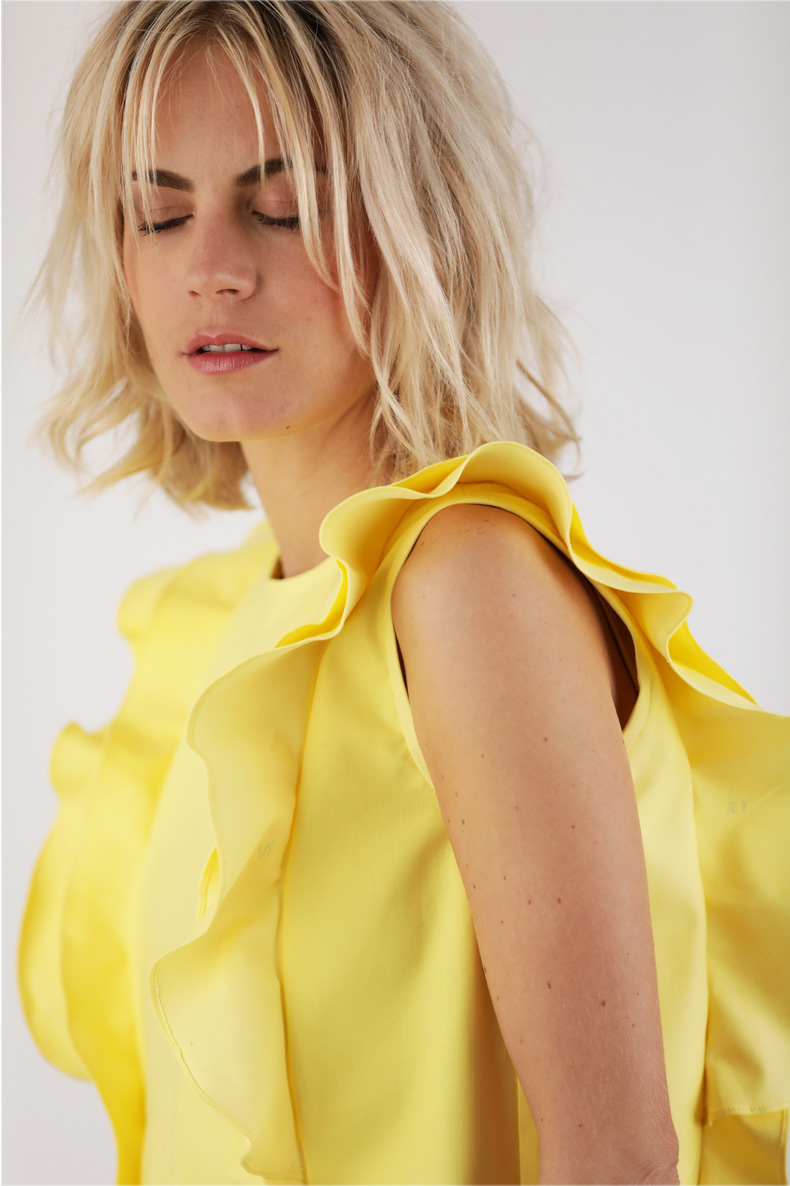 A close-up of a woman wearing a yellow top with ruffles.
