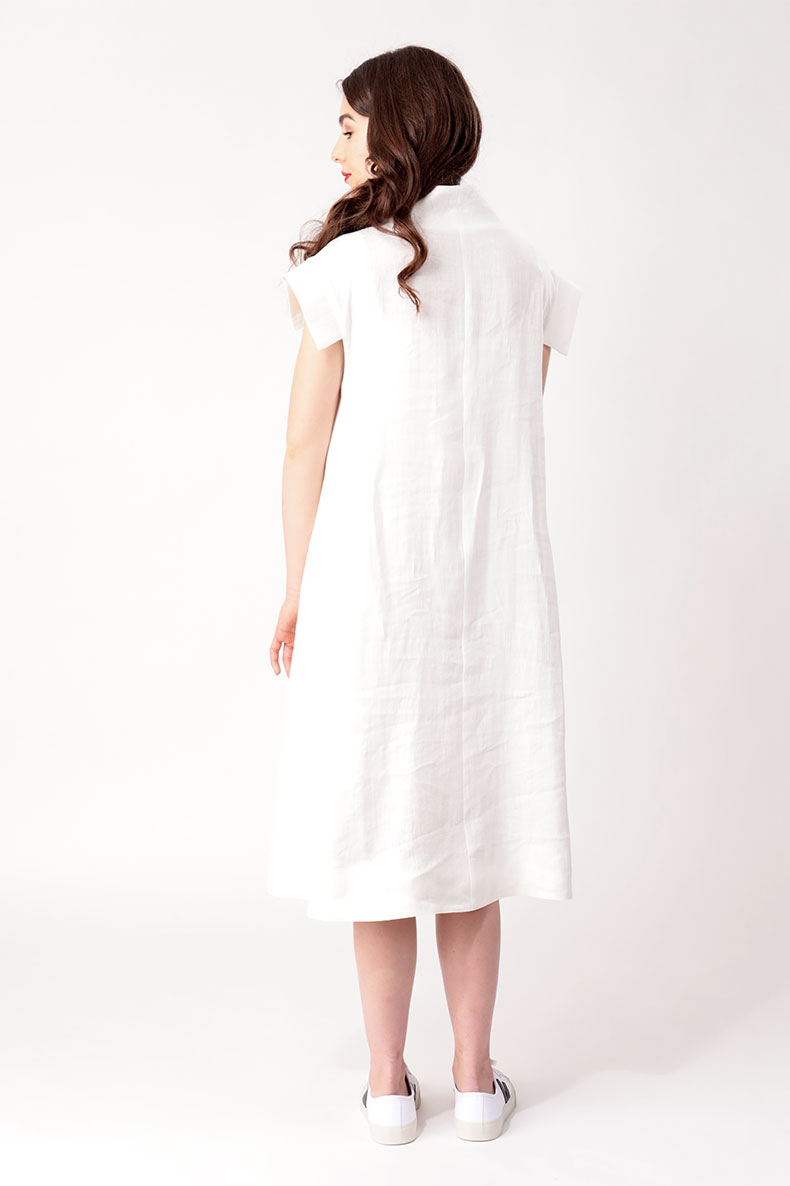 In front of a white wall, a woman with her back to the camera is wearing a white dress.