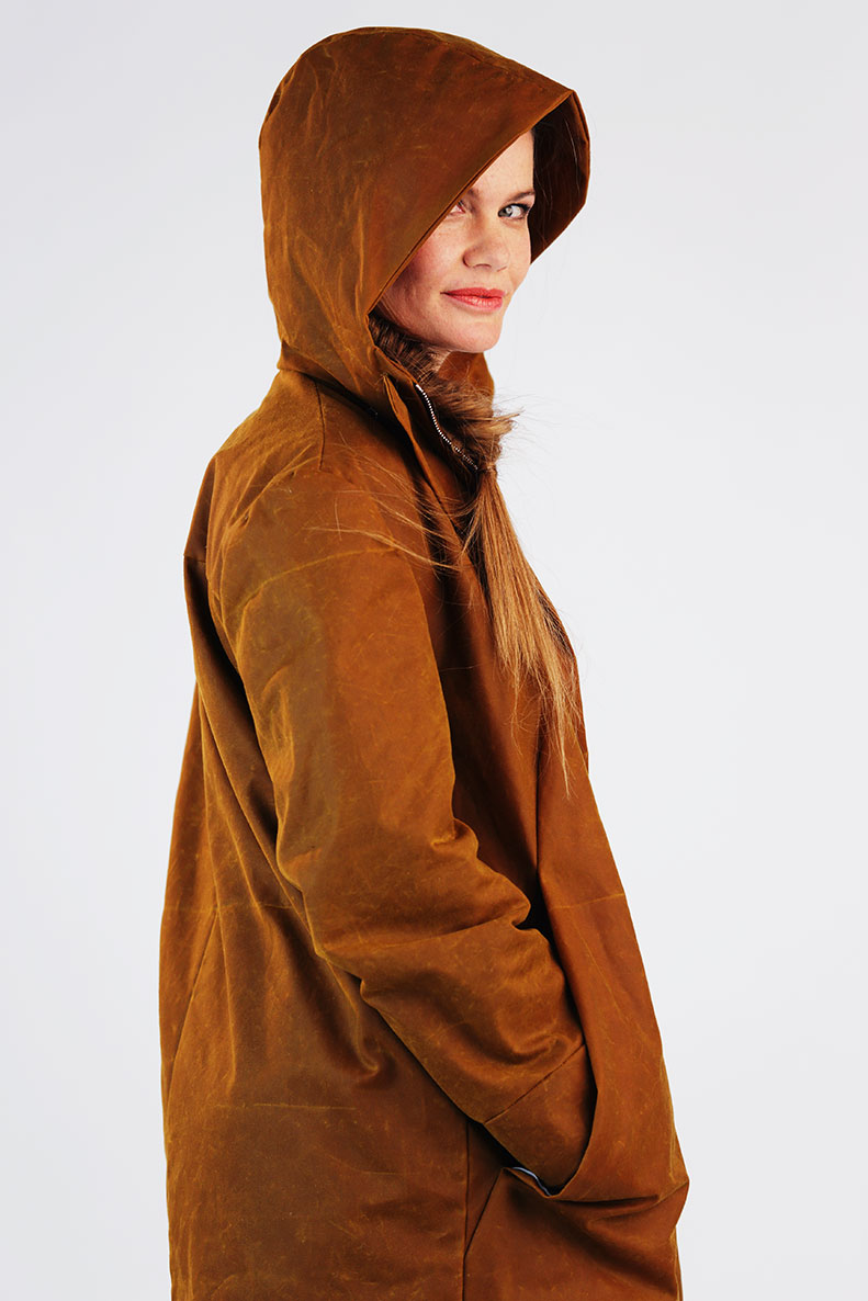 A woman is looking sideways with a smile through the hood of her self-sewn parka towards the camera.
