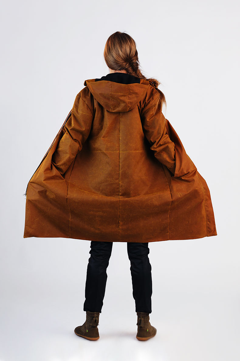 A woman with her back to the camera is unfolding her self-sewn anorak towards a white wall.