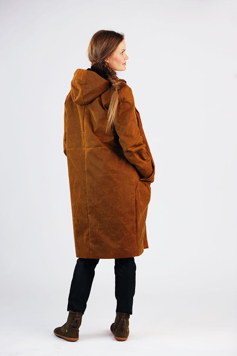A woman is standing with her back to the camera, wearing her self-sewn brown anorak.