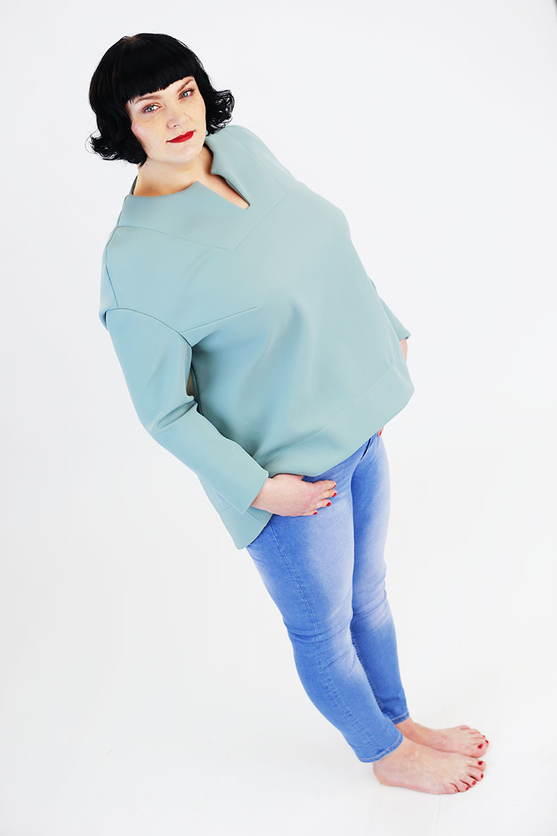A woman is standing diagonally on a white surface, wearing a turquoise shirt and light blue jeans.