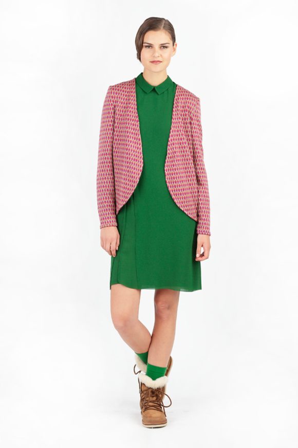 In front of a white background, a woman is standing and wearing a cardigan along with a green skirt.