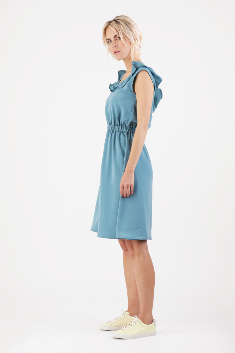 Eine Frau steht in einem blauen Kleid mit Rüschen.