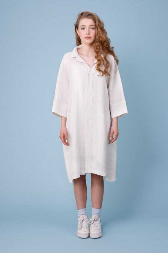 vor einem blauem Hintergrund posiert ein schlankes jugendliches Mädchen welches ein weißes Kleid trägt